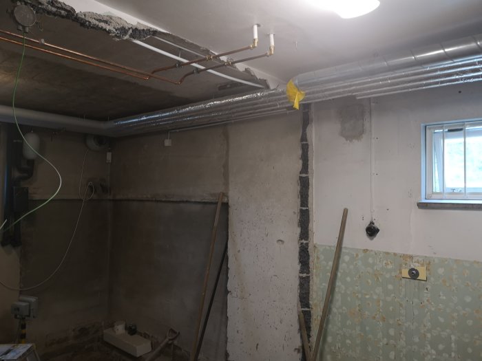 Renoveringsarbete i källare med synliga rör och ledningar, delvis rivna väggar och en kanalfläkt.