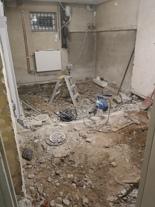 Rivningsarbete i rum med grus och stenar på golvet, stege och byggmaterial synliga.