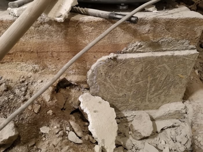 Rivningsarbete med synligt berg, rörledningar och uppbrutet betong på en byggarbetsplats.