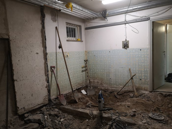 Pågående rivningsarbete i källare med verktyg, öppnat golv och expanderat kärl i bakgrunden.