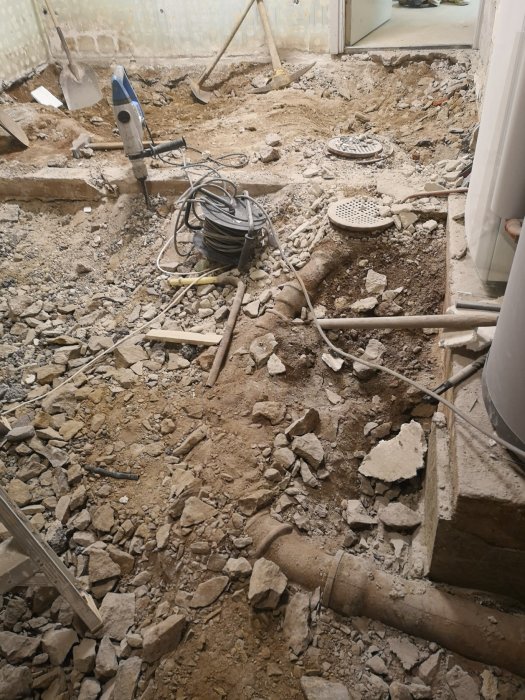 Rivningsarbete med synliga rör i betonggolv, sprängsten och verktyg, kanalfläkt vid sidan.