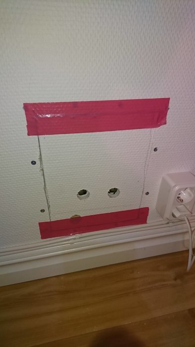 Vägg med temporär förslutning av rosa tejp och hål för PEX-slangdragning.