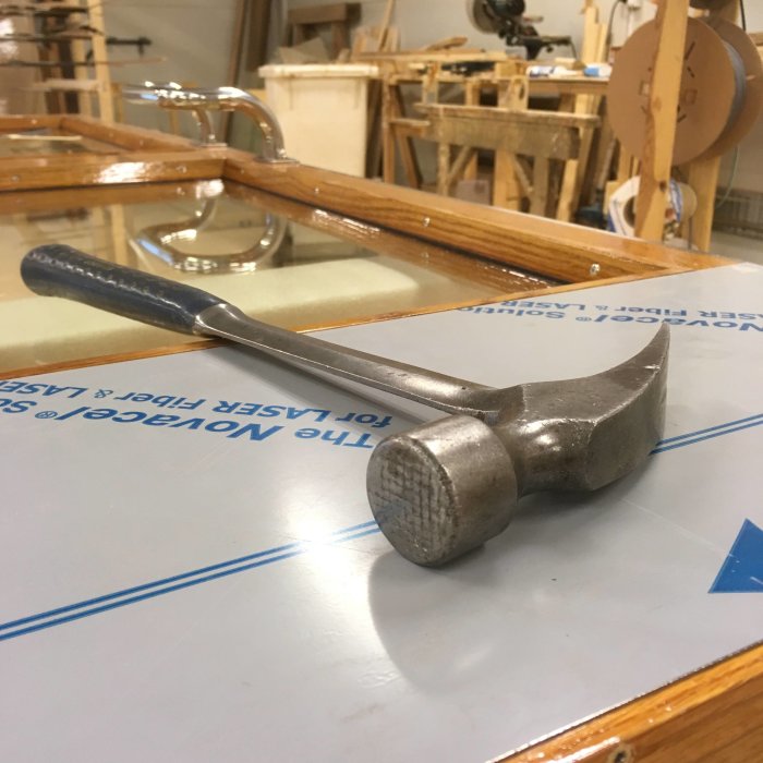 Hammer ligger på ett vit och blått ritbord i en snickeriverkstad.