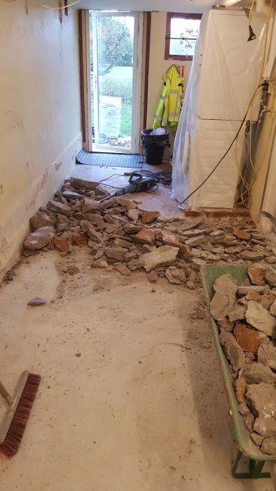 Renoveringsarbete på tvättstugans golv med borttagen betong och byggmaterial i skottkärra.