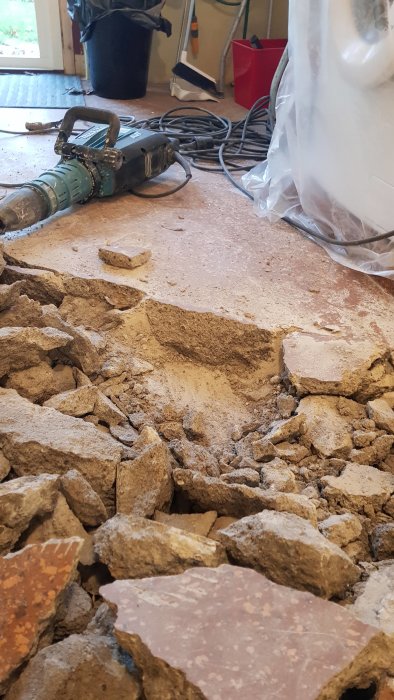 Uppbrutet golv i tvättstuga med betong och tegel i en hög och en borrhammare till vänster.