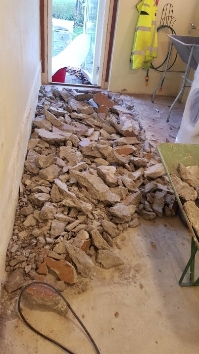 Uppbrutet betonggolv i tvättstuga med grushög och verktyg.