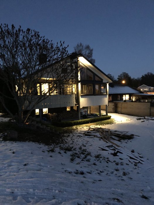Ett hus vid skymningen med tända utelampor och synligt skymningsrelä på utsidan. Snö ligger på marken.