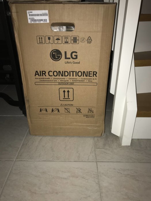 Förpackad LG Libero 12-enhet med texten "AIR CONDITIONER" på lådan står på ett golv.