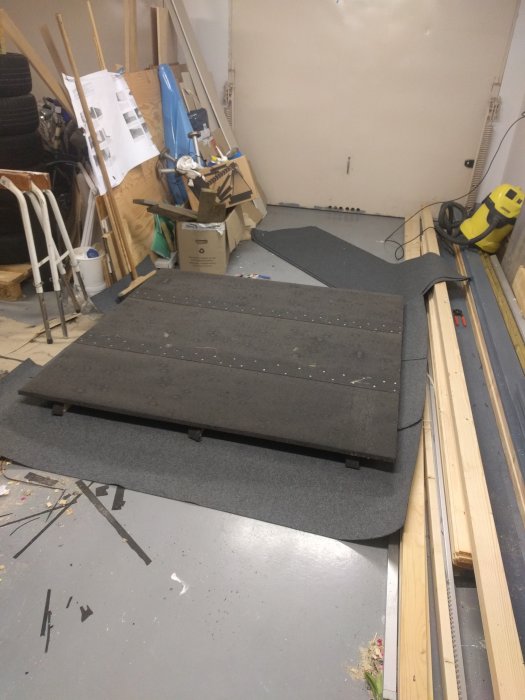 Takpapp som spikats på flera träbitar på golvet i ett rörigt garage.