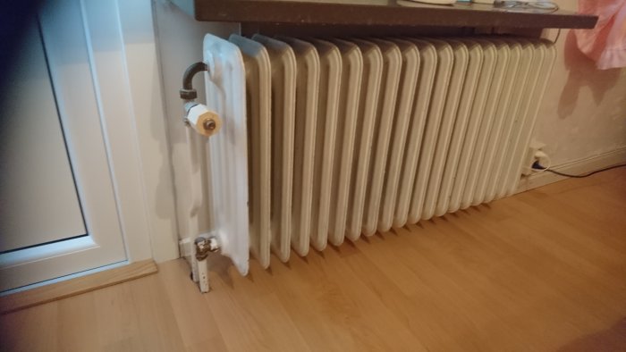 Vattenradiator med borttagen termostat som visar en pigg, placerad i ett rum vid ett fönster.