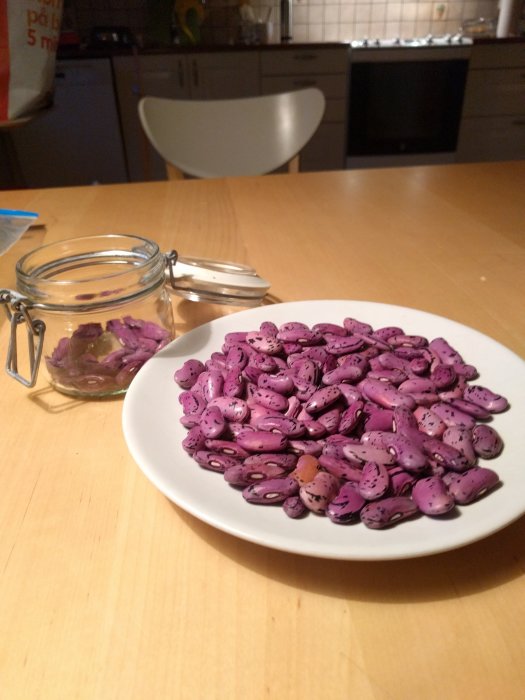 Tallrik med rosa-svarta rosenbönor på ett köksbord, öppen glasburk i bakgrunden.