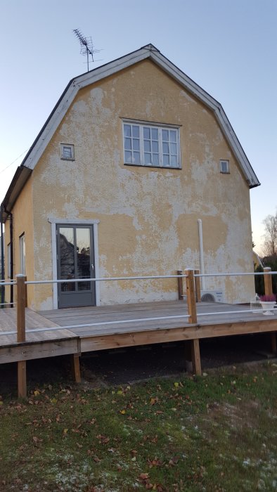 Äldre husfasad med flagnande färg och synlig slitage, stor veranda framför, i behov av renovering.