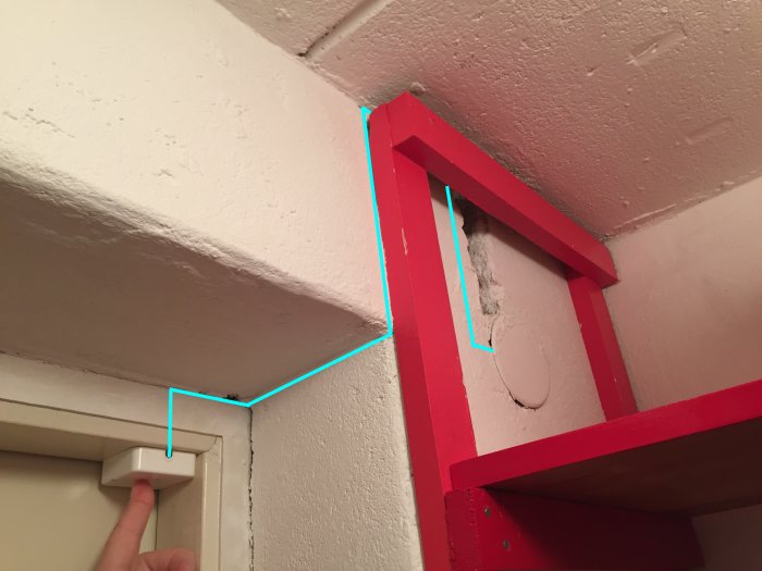 En hand trycker på en väggströmbrytare med en illustrerad blå linje som visar föreslagen kabeldragning.