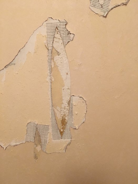 Nedriven tapet avslöjar spacklade hål med nätstruktur på en vägg.