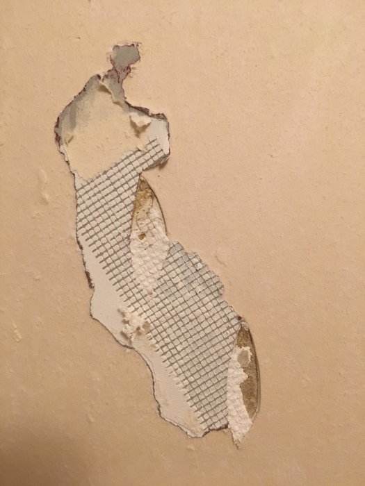 Ögonformat hål i vägg med synligt spackelnät och bortriven tapet.