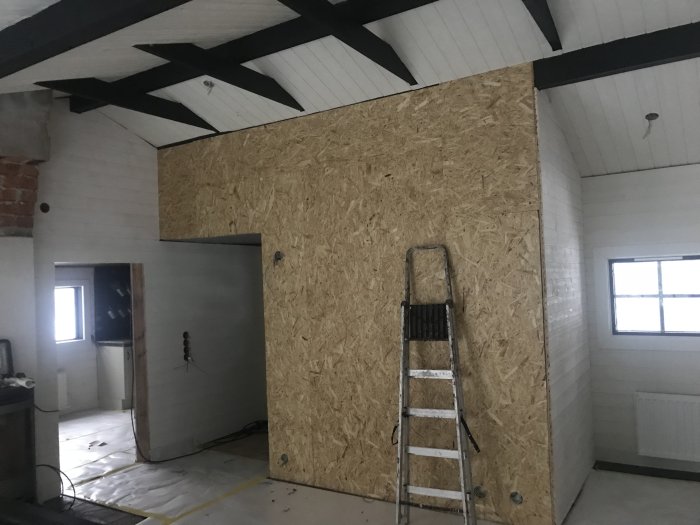 Renoverat vardagsrum och kök med osmålad OSB-fondvägg mot hall och aluminiumstege framför.