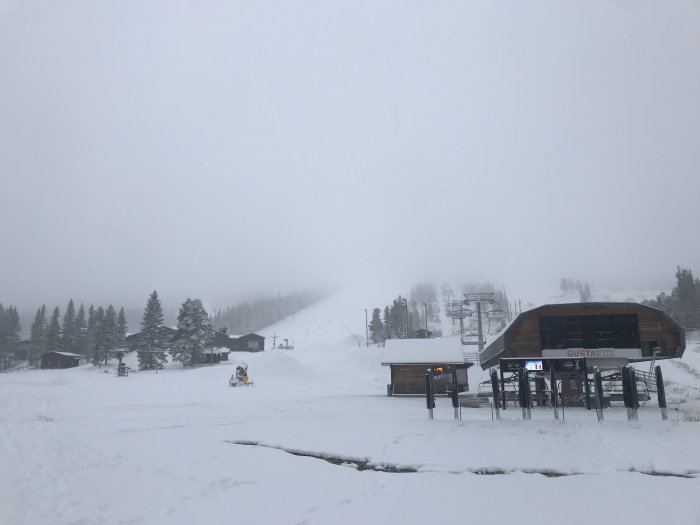 Täckt skidbacke med liftar under tung snöfall, synlighet är låg på grund av busväder.