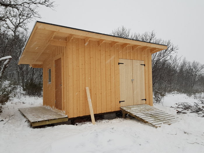 Nybyggt träskjul med ramp i snötäckt landskap, redo för vintern.