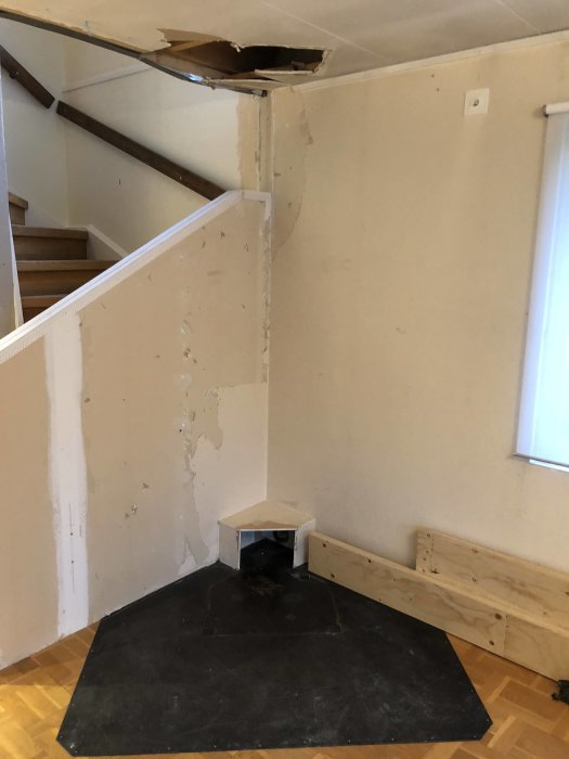 Hörn av ett rum före renovering med skadat golv och tak samt gammal kamin.
