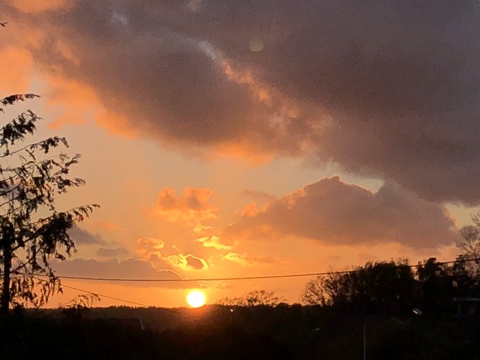 Solnedgång med solen lågt över horisonten och dramatiska rödorange moln mot en mörknande himmel.