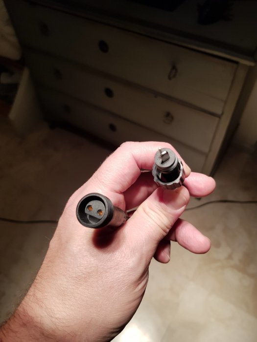 Hand håller en elektrisk adapter hittad i en låda.