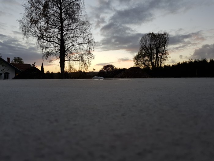 Nybetongerad garageplatta med skymd silhuett av träd och hus i bakgrunden vid solnedgång.