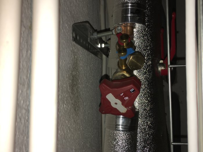 Närbild av rörinstallation med röd ventil som inte går att vrida, inklusive vita delar, mot en isolerad rörbakgrund.