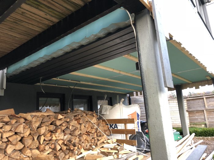 Ny panel under takutskjut vid uterum och vedstapel i förgrunden.