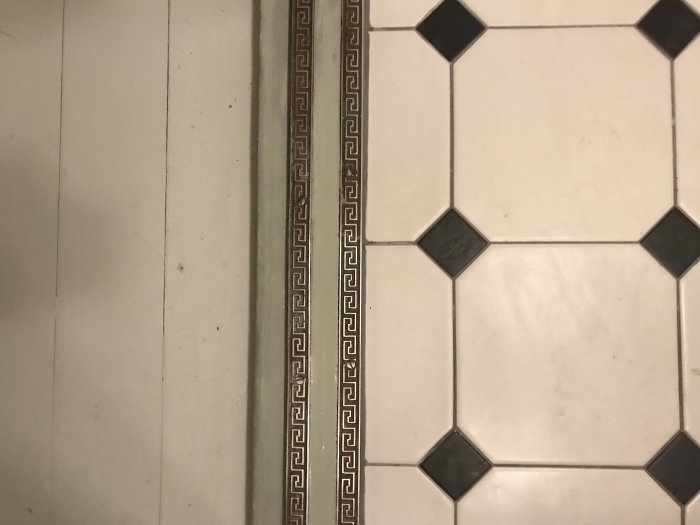 Renoverad tröskel med dekorativ list intill en vit och svart mönstrad kakelgolv.