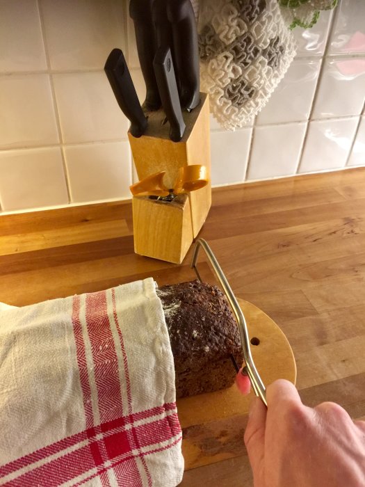 Hand som håller en bågfil skär genom ett bröd intill ett knivblock med slöa knivar.