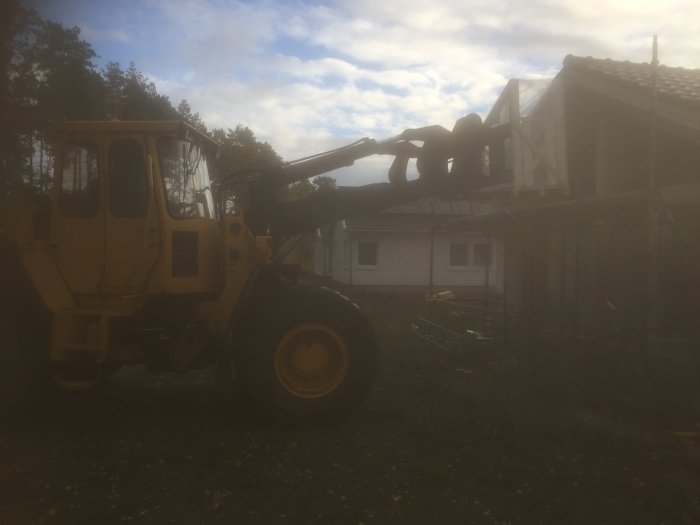 För svagt synbar gaffeltruck som hanterar stor glasparti vid montering på ett hus under konstruktion.