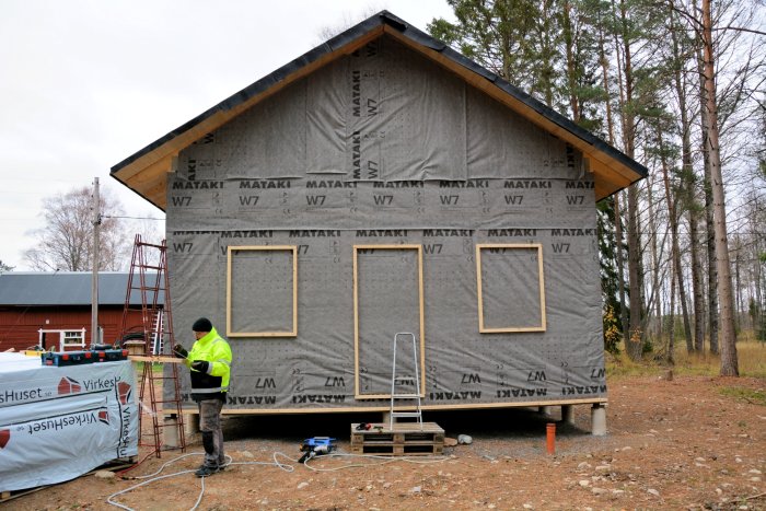 En person vid ett hus under konstruktion med uppsatta isoleringsskivor och läkt på gavelväggen.