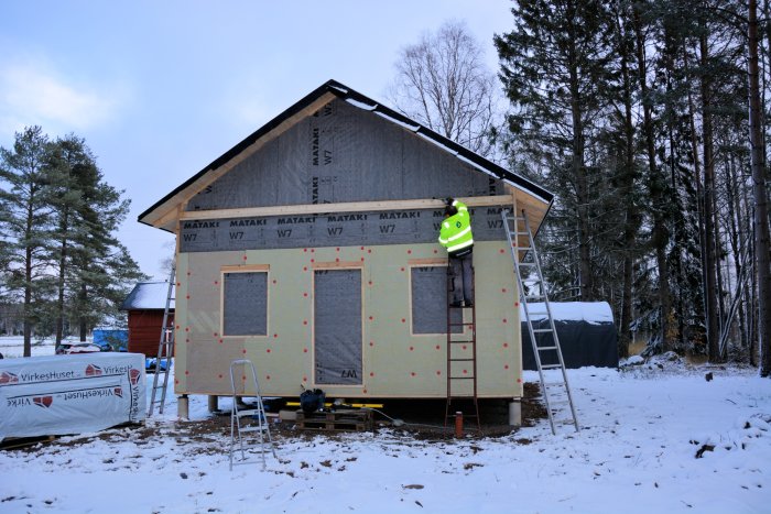 Utvändig isolering installeras på ett hus i snölandskap, med person på stege.
