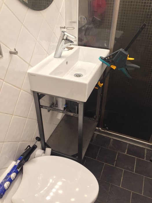 Installation av badrumsmöbel med handfat och kran, verktyg syns, ej färdigställt.