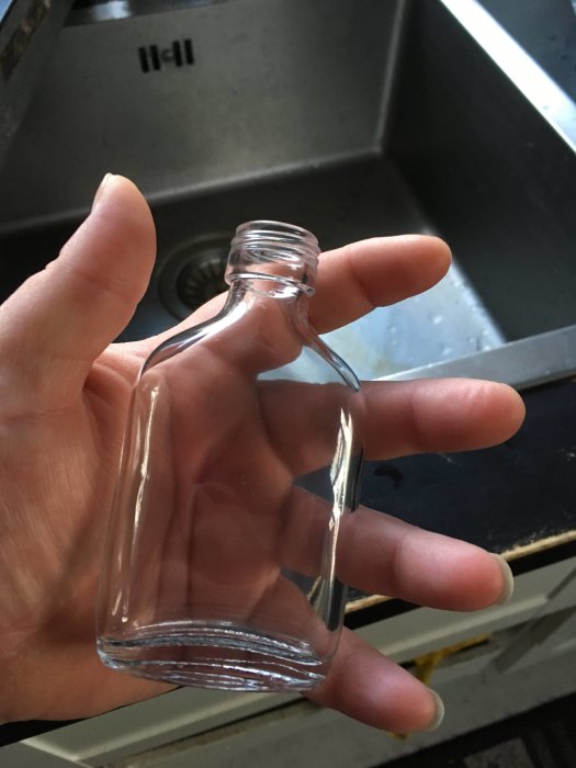 Hand håller en tom liten glasflaska avsedd för "hot sauce".