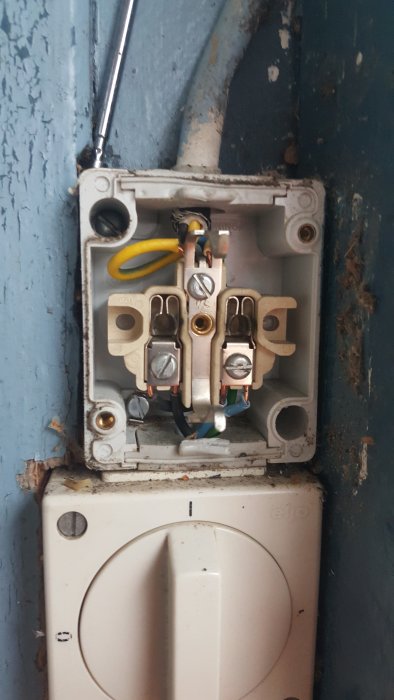 Öppnat elfack som visar en ojordad vägguttagsinstallation med synliga ledningar och anslutningar inuti en byggnad.