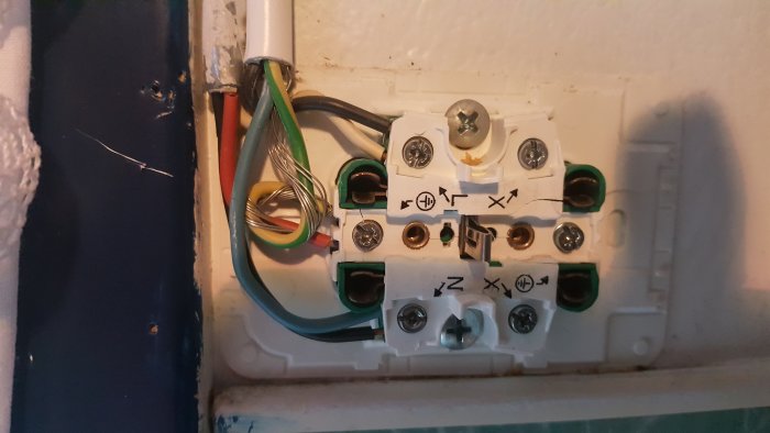 Öppet eluttag med synliga ledningar och anslutningar; färgkodade kablar anslutna till uttagets terminaler.