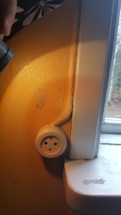 Ojordat eluttag vid ett fönster med sliten färg och synlig sladd.