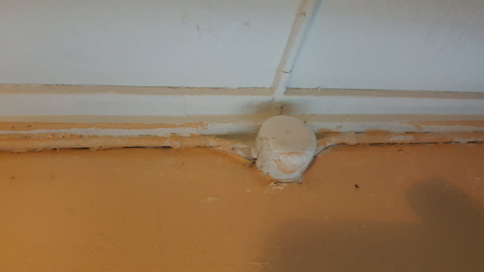 Ommålat, gammalt eluttag på en vägg, kablar dolda med klumpig spackling längs sockeln.