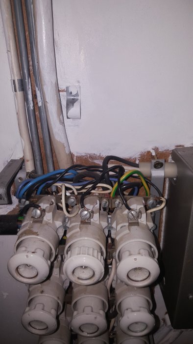 Ett öppnat eluttag med exponerade ledningar och anslutna säkringar på en vägg, indikation av elektriska arbeten i ett gammalt hus.