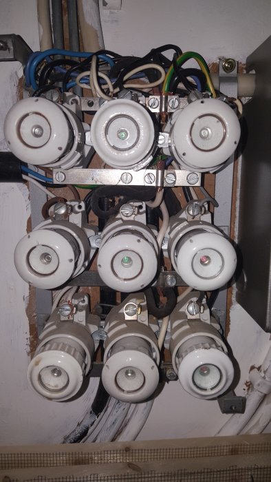 Elskåp med flera keramiska säkringar och intrasslade kablar, behov av elektrikers bedömning.