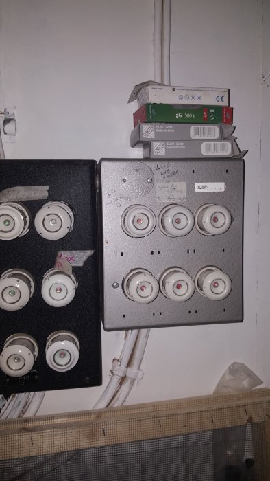 Elskåp med säkringar och plintar, handskrivet etiketter, kablar och installationsmaterial vid en vit vägg.