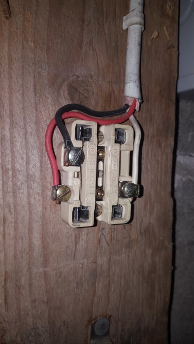 Öppnat gammalt eluttag utan synlig jordning, visande ledningar och skruvanslutningar på en trävägg.