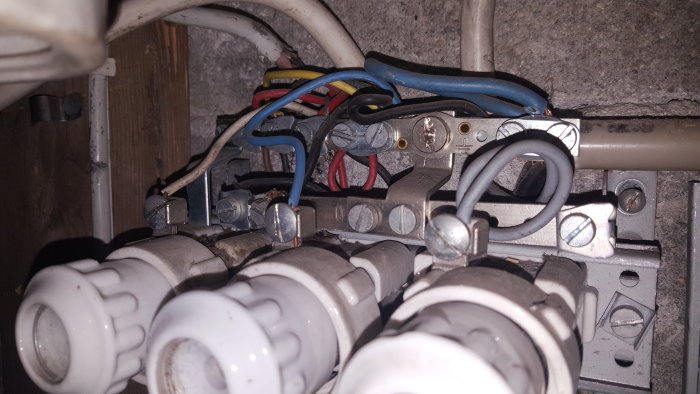 Elskåp med flera inkopplade keramiska säkringar och trassliga elektriska kablar i ett gammalt hus.