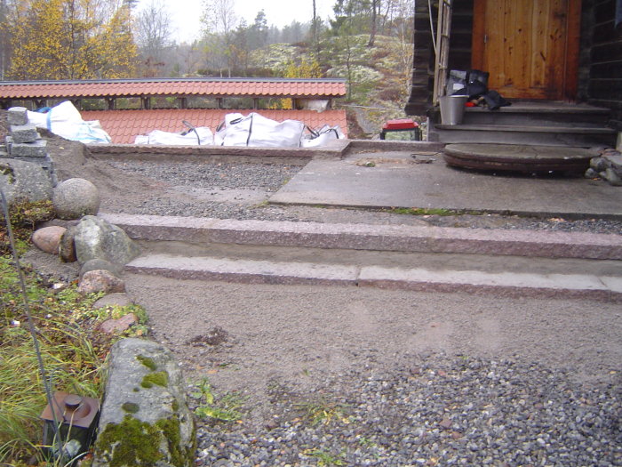 Nybyggda betongtrappsteg som leder upp till en träveranda med byggmaterial i bakgrunden.