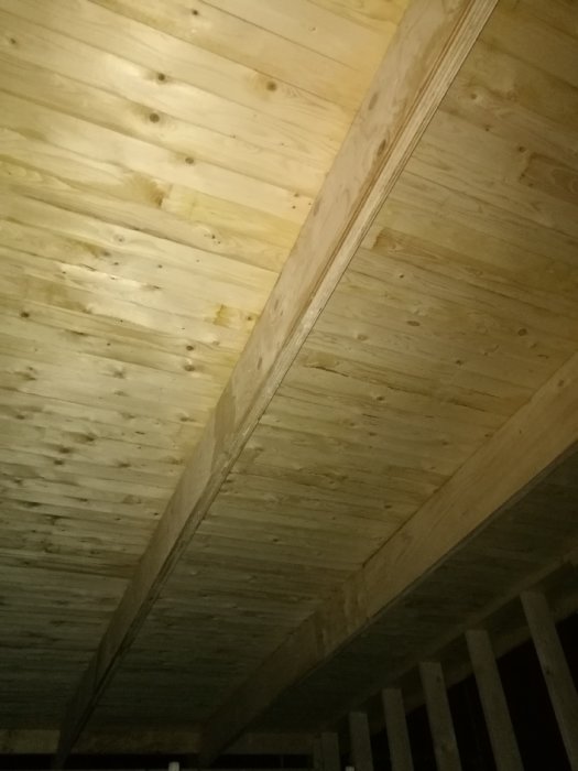 En hemmagjord limträbalk av plywood under ett råsponttak med synliga skarvar och limfogar.