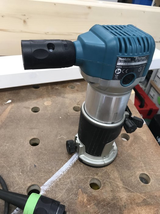 Makita överfräs RT0700C på arbetsbänk med ansluten strömkabel och spår i träplattan.