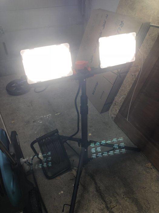 Två LED-arbetslampor tända och monterade på ett stativ i ett garage.