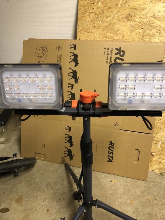 Två LED-arbetslampor monterade på stativ framför kartonger i ett garage.
