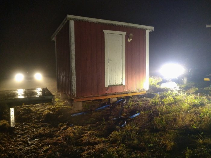 Förråd på grunden i natt mörker med bilens strålkastare lysande i bakgrunden.